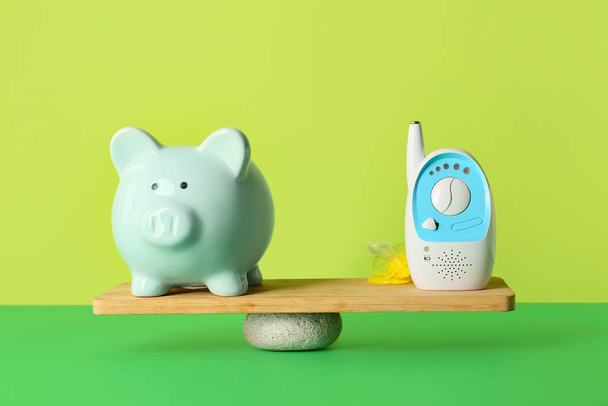 Piggy bank with baby monitor on teeterboard against color background. Concept of balance - Photo, Image