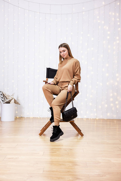 Mladá modelka v pleteném obleku, béžové kožené boty a svetr pózující uvnitř - Fotografie, Obrázek