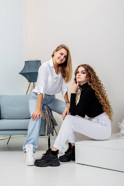 Two young beautiful women in trousers and a sweater, in leather boots on their feet. New collection of women's boots - 写真・画像