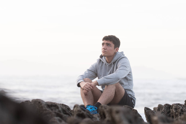 Thoughtful hispanic teenager sitting outdoors on rocks. Depression and anxiety in adolescence concept - Fotoğraf, Görsel