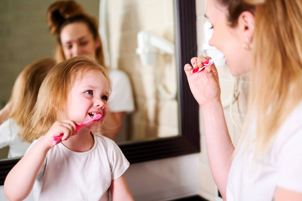 Mother and daughter brushing their teeth at home - Fotoğraf, Görsel
