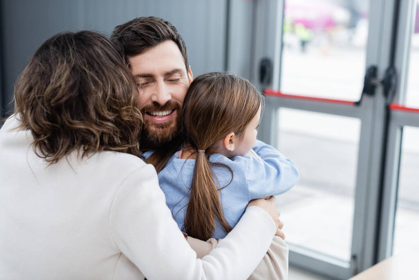 Mutlu sakallı adam havaalanında ailesine sarılıyor.  - Fotoğraf, Görsel