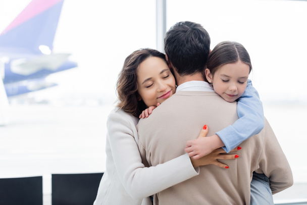 happy woman and daughter hugging man in airport  - Foto, Imagen
