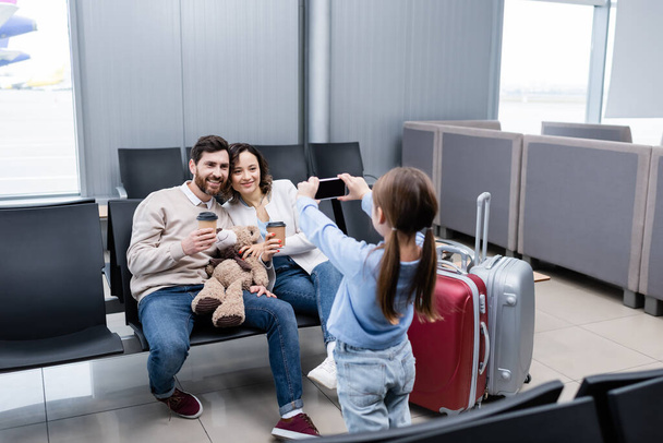 kid taking photo of happy parents with paper cups in airport lounge  - Foto, Bild