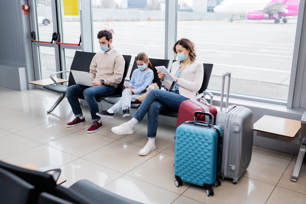parents and kid in medical masks using gadgets in airport - Fotó, kép