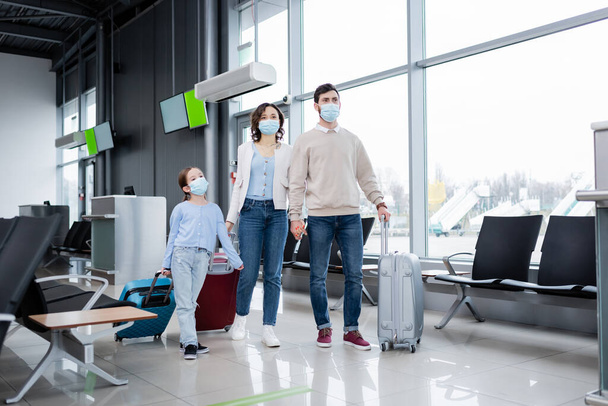 family in medical masks walking with luggage in airport lounge  - 写真・画像