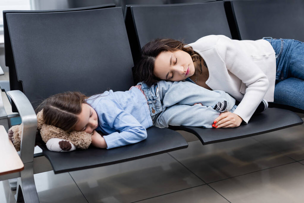 moeder en dochter slapen op vliegveldstoelen in de vertrekhal  - Foto, afbeelding