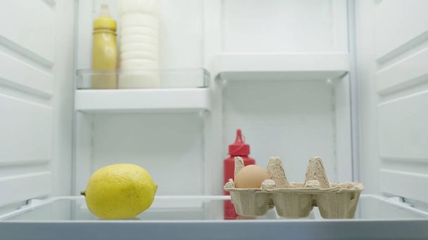 whole lemon, egg, bottles with mayonnaise, mustard and tomato sauce in refrigerator - Foto, Imagem
