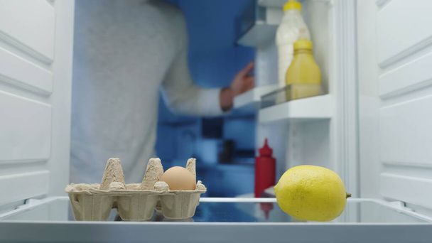 vue recadrée de l'homme flou près des œufs, du citron et des sauces au réfrigérateur - Photo, image