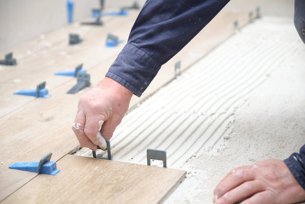 Arbeiders handen leggen keramische hout effect tegels met behulp van tegel levelers. - Foto, afbeelding