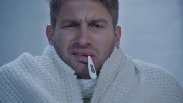 displeased sick man with thermometer in mouth measuring temperature at home - Photo, Image
