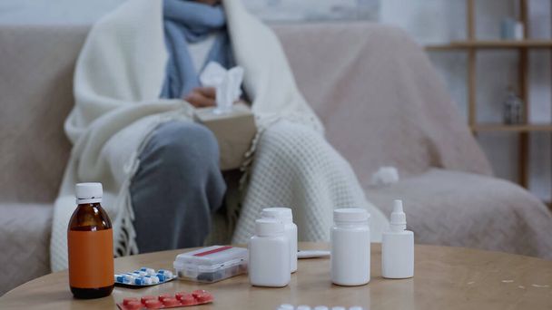cropped view of blurred sick man sitting near medicaments on table - Foto, imagen