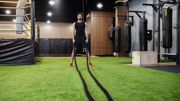 full length of bearded man working out with battle ropes - Foto, Bild