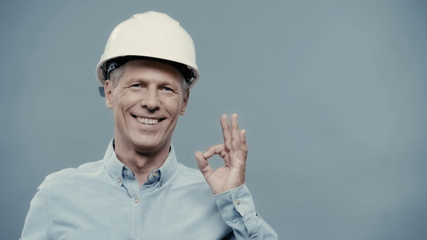 Smiling engineer in hardhat showing okay gesture isolated on grey  - Foto, immagini