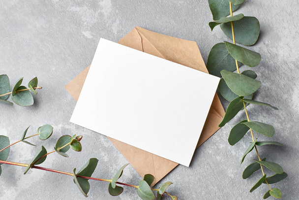Invitation or greeting card mockup with fresh eucalyptus twigs on grey concrete background, copy space, top view - Foto, afbeelding