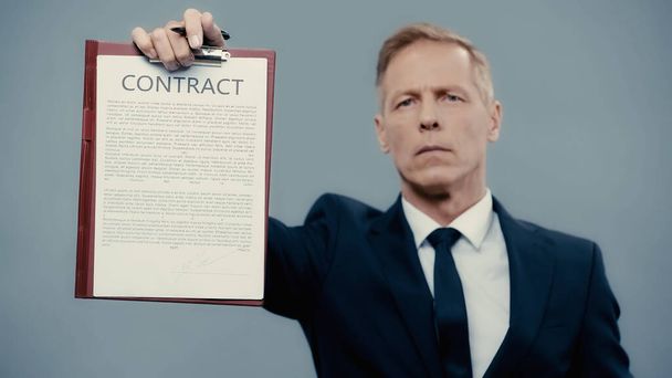Contract on clipboard in hand of blurred businessman isolated on grey  - Foto, Bild