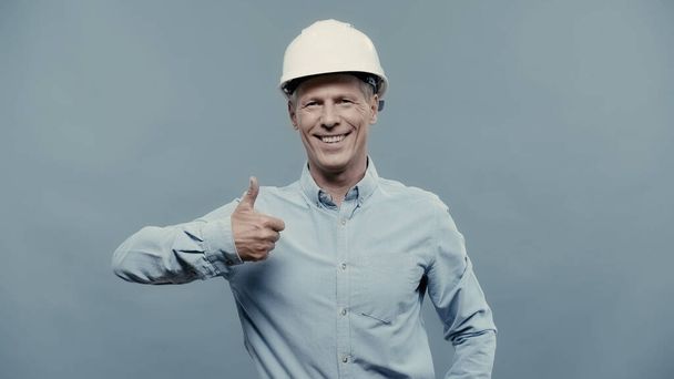 Smiling engineer in hardhat showing like isolated on grey  - Фото, изображение