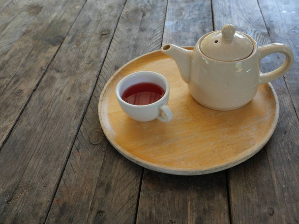 Červený čaj Květní lístky růže v bílém šálku a keramické konvice na dřevěném podnosu na hnědém stole - Fotografie, Obrázek