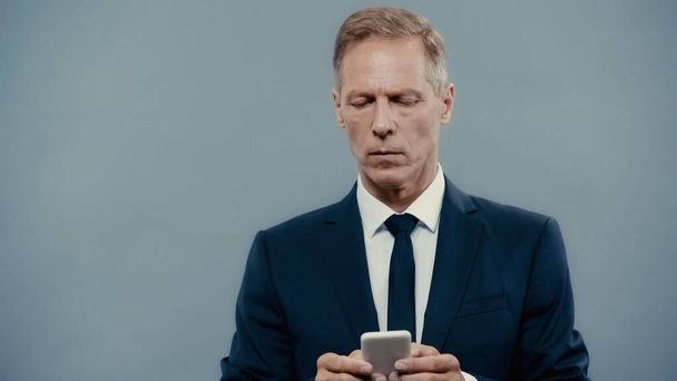 Mature businessman in suit chatting on smartphone isolated on grey  - Foto, Imagen