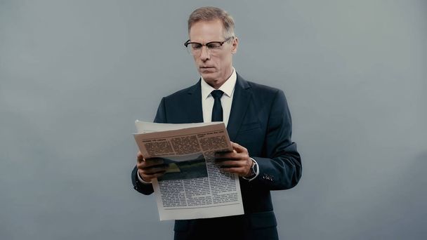 Mature manager in eyeglasses reading news isolated on grey  - Photo, Image