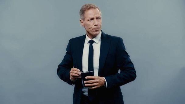 Businessman holding drinking flask and looking away isolated on grey  - Valokuva, kuva