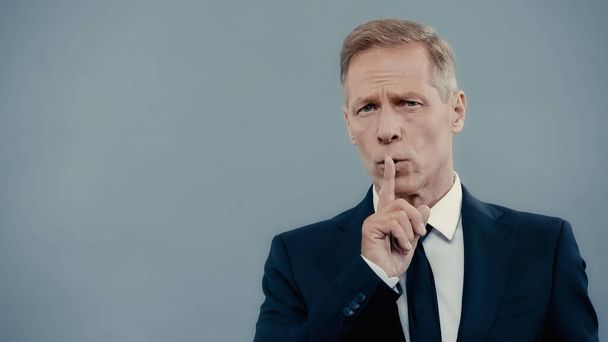Mature businessman showing secret gesture isolated on grey  - Foto, afbeelding