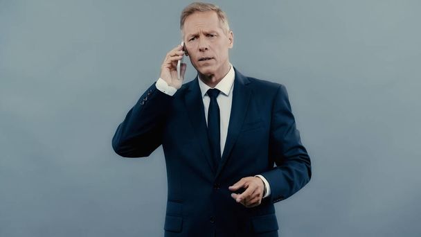Stressed businessman talking on cellphone isolated on grey  - Photo, image