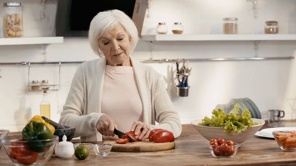 senior woman cutting bell pepper near fresh vegetables on kitchen table - Fotoğraf, Görsel