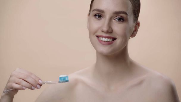 smiling woman with bare shoulders holding toothbrush with toothpaste isolated on beige  - Foto, immagini