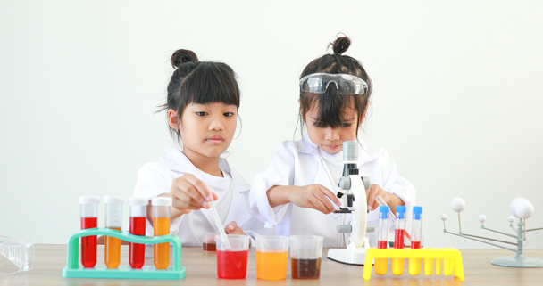 Little girl asian cute little student child learning research and doing a chemical experiment while making analyzing and mixing liquid in test tube at home on the table. - Fotó, kép