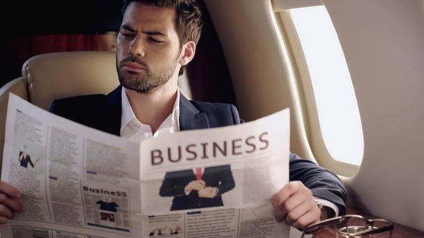 Επιχειρηματίας ανάγνωση εφημερίδα κοντά γυαλιά ηλίου σε ιδιωτικό αεροπλάνο  - Φωτογραφία, εικόνα