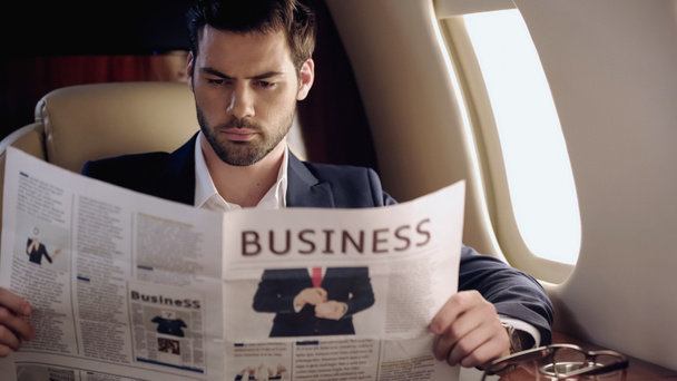 Bearded businessman reading news near eyeglasses in private plane  - Photo, image