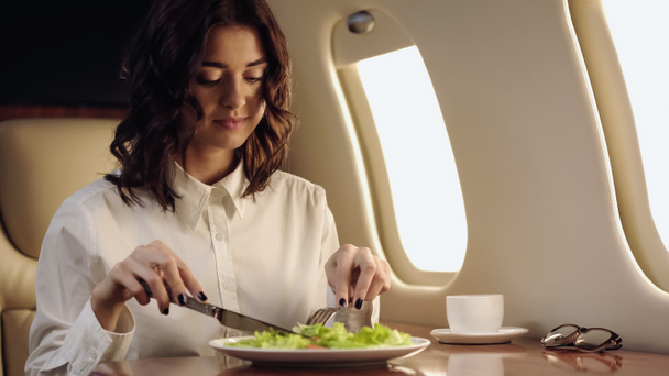 Young businesswoman holding cutlery near salad and coffee in private plane  - Foto, Imagem