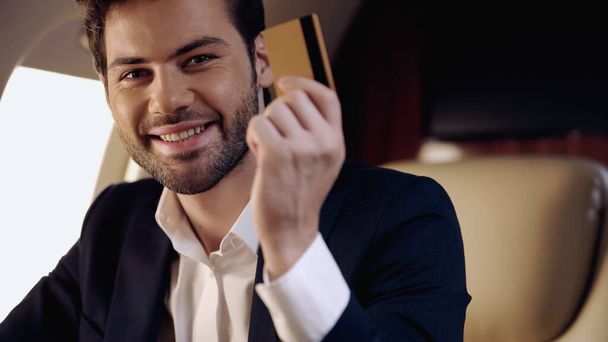Smiling businessman holding credit card in private jet  - Фото, изображение