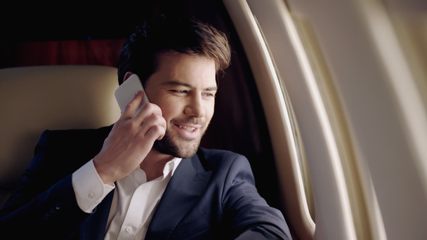 民間の飛行機の中でスマートフォンで話している間、ビジネスマンは微笑む  - 写真・画像
