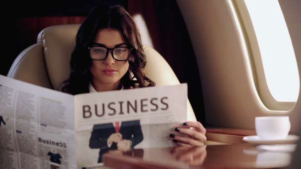 Businesswoman reading news near cup of coffee on table in private plane  - Valokuva, kuva