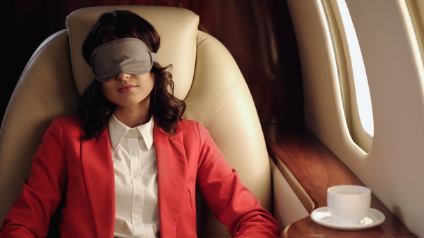 Businesswoman in sleep mask sitting near coffee cup in private plane  - Фото, изображение