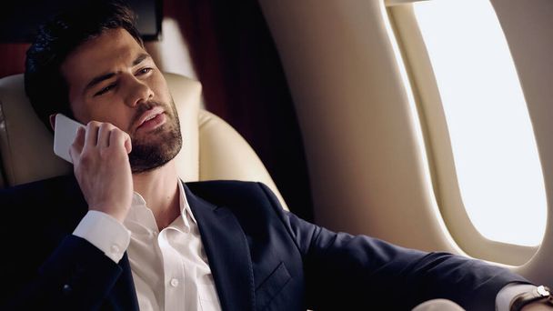 Businessman in suit talking on smartphone in private plane  - Fotó, kép