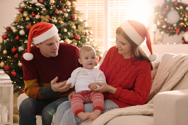 Happy couple with cute baby on sofa in room decorated for Christmas - Фото, изображение