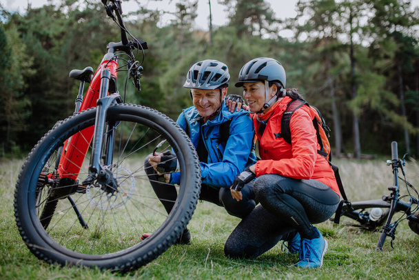 Active senior couple mending bicycle outdoors in forest in autumn day. - Foto, immagini