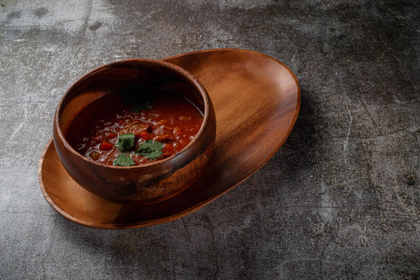Meat stew with parsley greens in a wooden bowl on a tray with bread crumbs against a gray stone table  - Zdjęcie, obraz