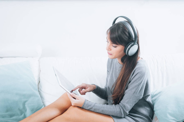 Brunette young woman listening to music with digital tablet and relaxing while sitting on sofa close up - Foto, Imagem