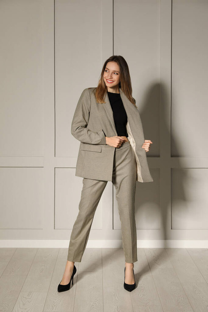 Full length portrait of beautiful young woman in fashionable suit near light grey wall indoors. Business attire - Zdjęcie, obraz