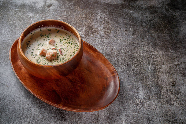Fish cream soup of salmon with herbs in a wooden bowl on a tray against a gray stone table  - Photo, image