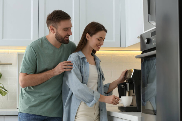 Happy couple preparing fresh aromatic coffee with modern machine in kitchen - Fotó, kép