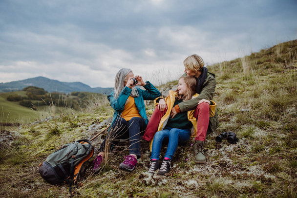 Ανώτερη γυναίκα φωτογραφίζει την κόρη της και την εγγονή της στην κορυφή του λόφου την ημέρα του φθινοπώρου. - Φωτογραφία, εικόνα