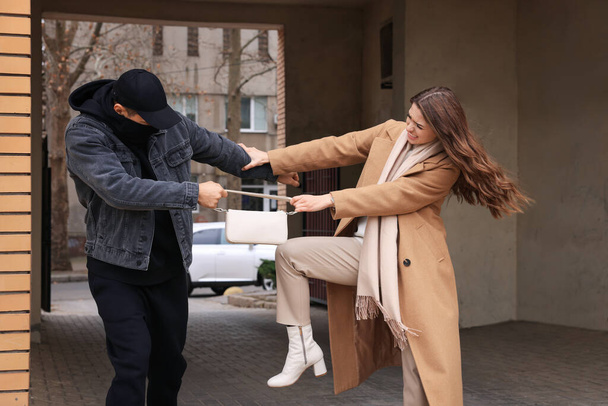 Woman fighting with thief while he trying to steal her bag in alley. Self defense concept - Foto, imagen