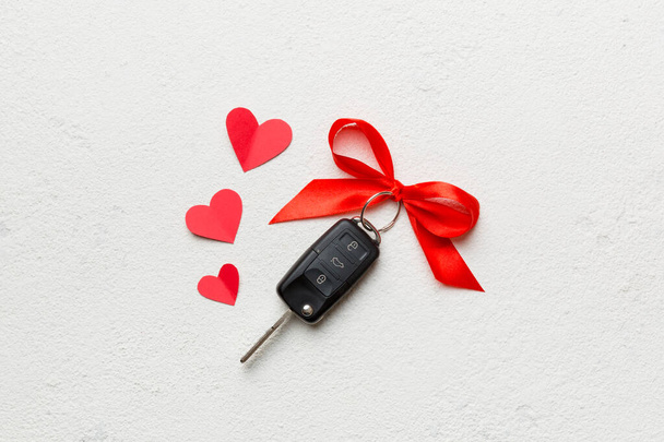 色の背景にリボンと赤の心を持つ現在のボックス内の黒い車のキー。バレンタインデーの構図｜Top view. - 写真・画像