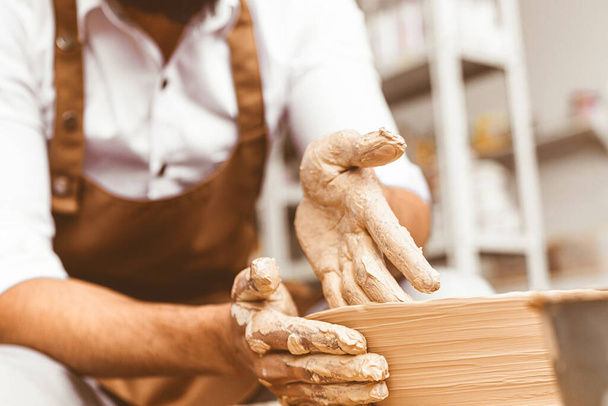A young male potter works in his workshop on a potters wheel and makes clay products. Close-up of hands - Foto, afbeelding
