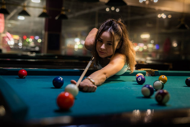 Young happy girl holding cue and play billiard at pub. lifestyle - Фото, изображение
